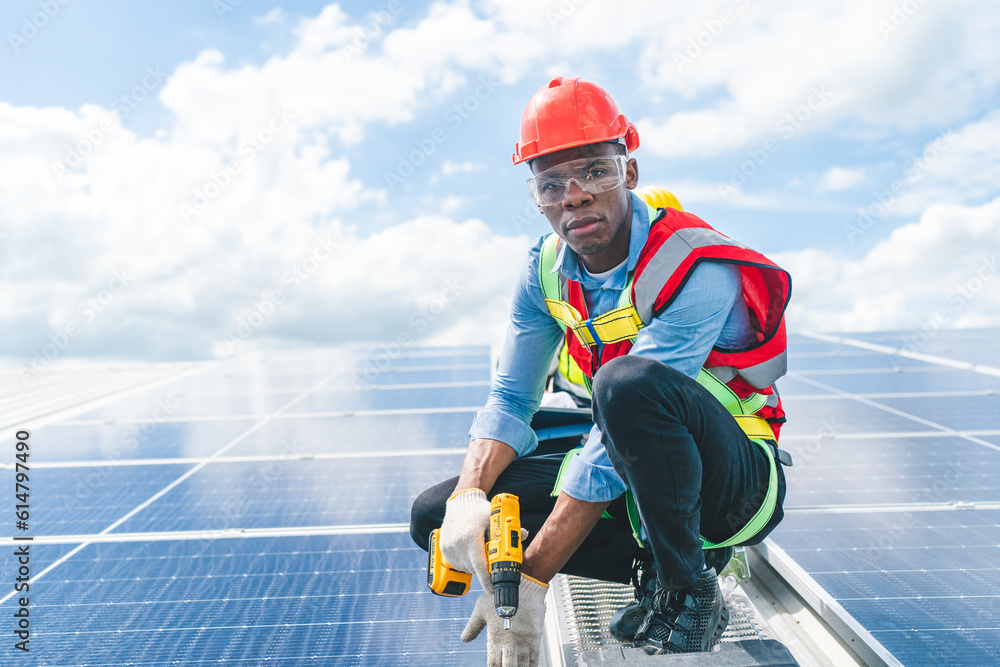 African American engineer maintaining solar cell panels on factory building rooftop. Technician working outdoor on ecological solar farm construction. Renewable clean energy technology concept African American engineer maintaining solar cell panels on factory building rooftop. Technician working outdoor on ecological solar farm construction. Renewable clean energy technology concept