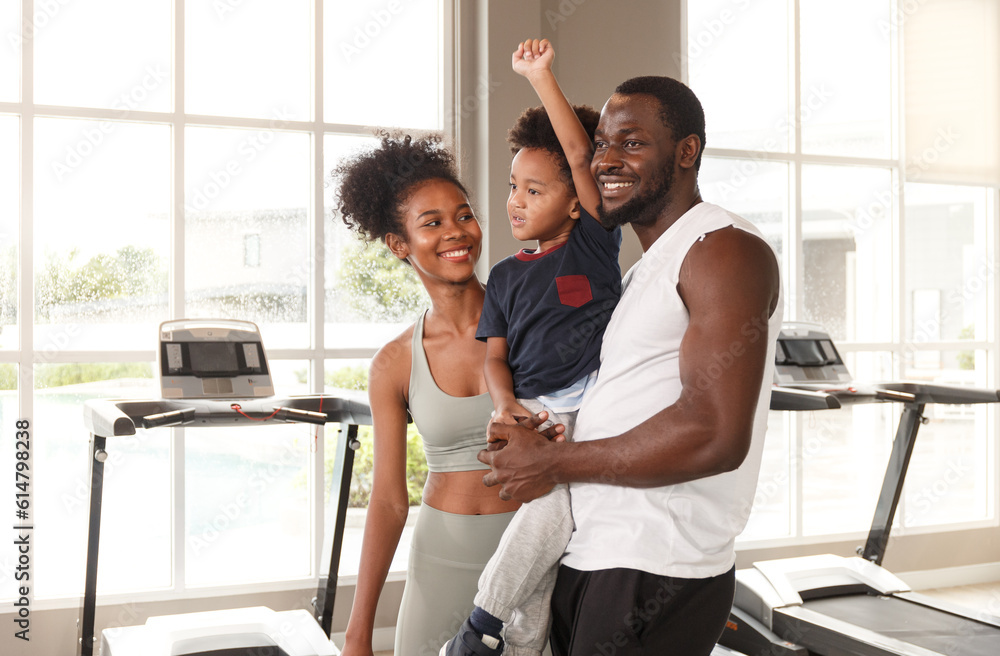 Young african american family in sportswear holding cute baby while exercising in the gym