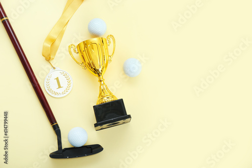 Gold cup with first place medal, golf club and balls on yellow background photo