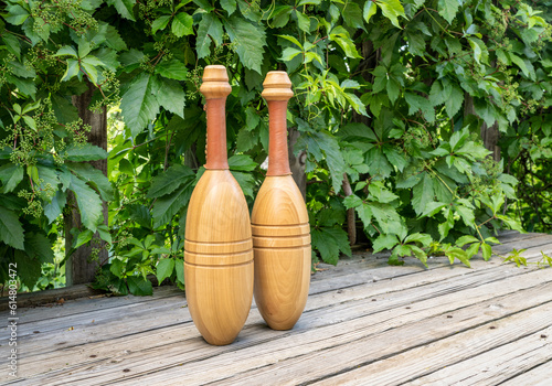 pair of wooden Indian exercise clubs on a wooden deck against green vine photo