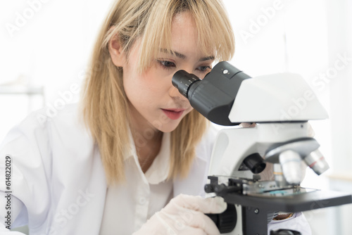 Asian woman scientist looking through microscope doing analysis and test sample in the laboratory