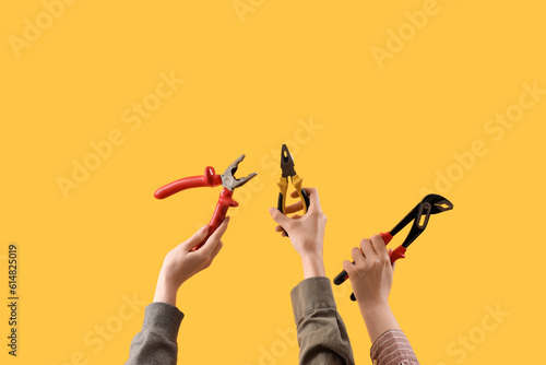 Female hands holding different pliers on yellow background photo