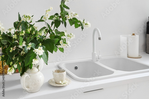 Vase with blooming jasmine flowers  teapot and cup of tea on white kitchen counter