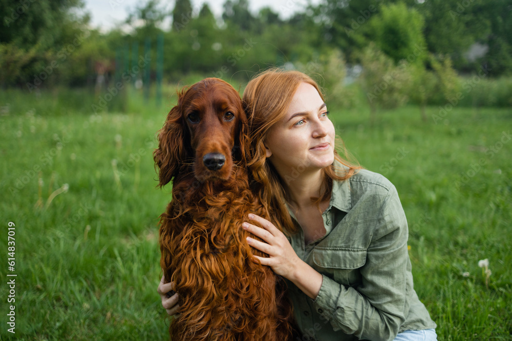 Beautiful woman hugging and kissing Irish Setter dog. Dog and owner together outdoors. Love and friendship between dog and owner in park. true friends forever, people pets concept