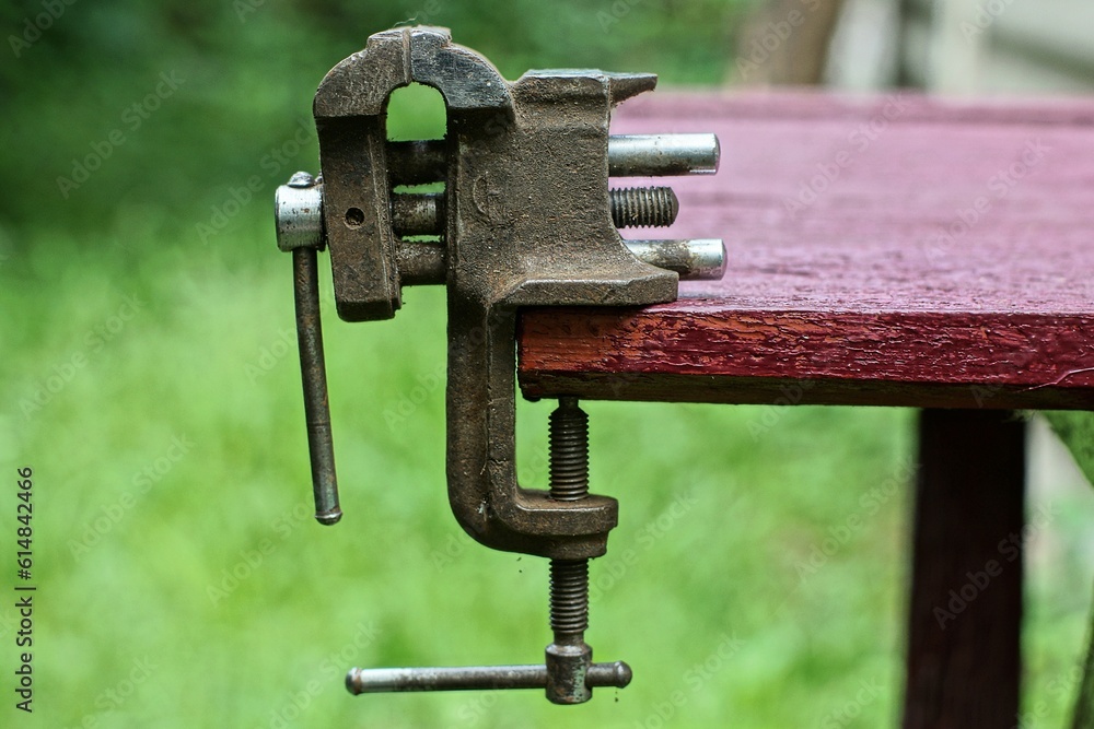 small iron rusty mechanical very old dirty retro vise for working with metal stands on a brown desktop on the street during the day small iron rusty mechanical very old dirty retro vise for working with metal stands on a brown desktop on the street during the day