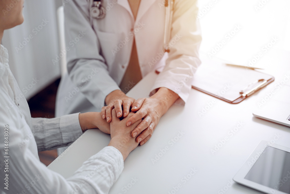 Obraz premium Doctor and patient sitting at the desk in clinic office. The focus is on female physician's hands reassuring woman, close up. Perfect medical service, empathy, and medicine concept