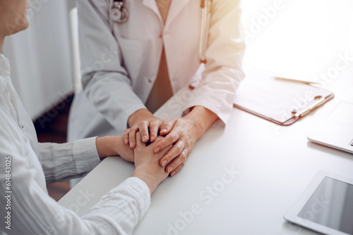 Doctor and patient sitting at the desk in clinic office. The focus is on female physician s hands reassuring woman  close up. Perfect medical service  empathy  and medicine concept