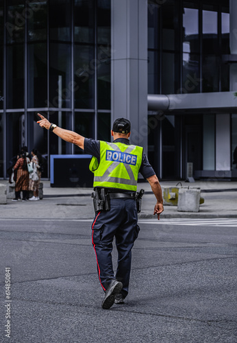 Police man is directing traffic during the rush hour in down town Toronto. Police man regulating traffic on city street.