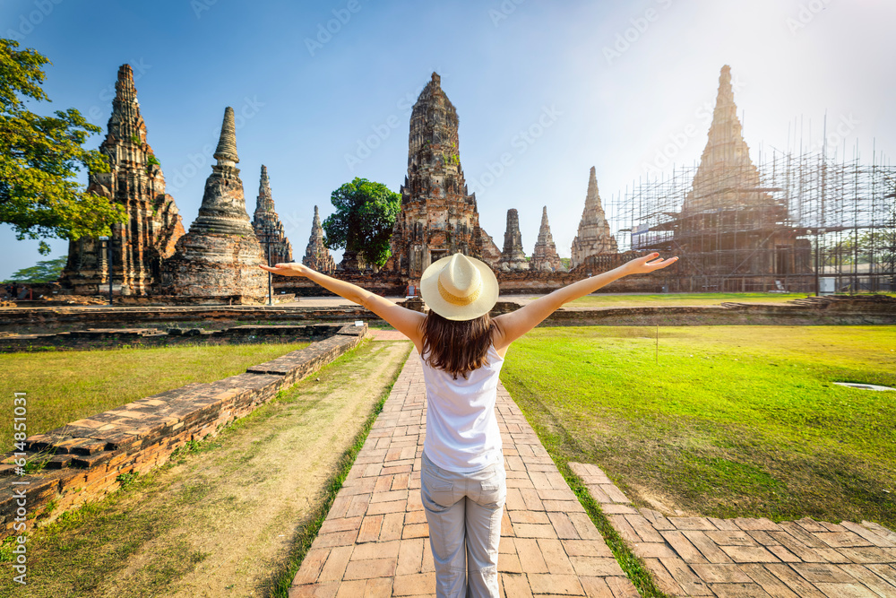 A excited tourist woman on a sightseeing trip stands in front of the buddhistic temple ruins at the historic city of Ayutthaya, Thailand