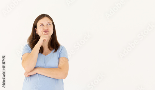 Portrait of standing with thoughtful serious smart expression, pondering answer, having doubts and suspicion, wearing blue T-shirt pregnant woman. Indoor studio shot isolated on white background.
