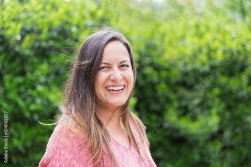 Outdoor portrait of a laughing 45 year old woman with windblown brown hair looking at the camera in the park on a sunny day. Confidence and tranquility of a mature woman. Happiness, lifestyle.