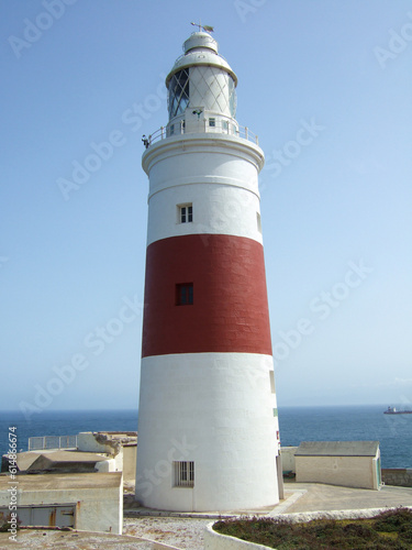 Red and white lighthouse on Spanish Atlantic coast with sea view and some ships in background