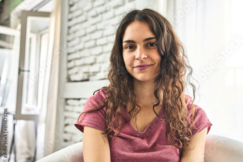 A young Caucasian woman, sitting in a cozy armchair in her home, happily enjoying the morning with contentment.