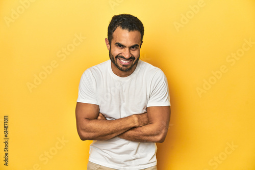 Casual young Latino man against a vibrant yellow studio background, laughing and having fun.