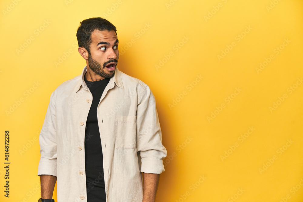 Casual young Latino man against a vibrant yellow studio background, being shocked because of something she has seen. Casual young Latino man against a vibrant yellow studio background, being shocked because of something she has seen.