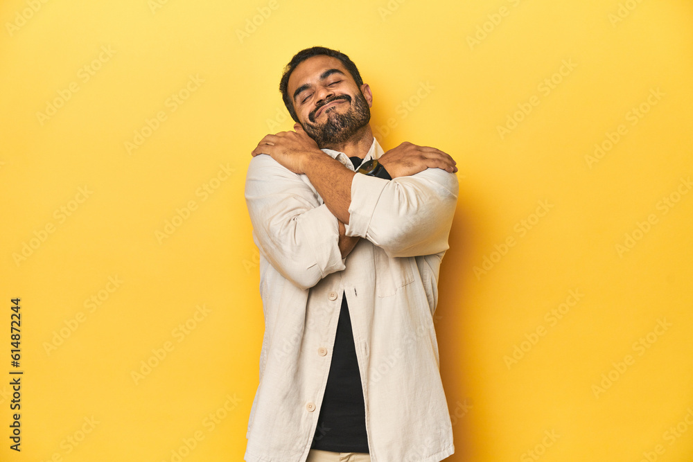 Casual young Latino man against a vibrant yellow studio background, hugs, smiling carefree and happy. Casual young Latino man against a vibrant yellow studio background, hugs, smiling carefree and happy.