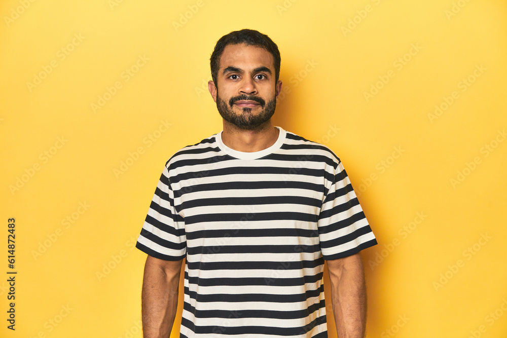 Smiling young Latino man in black striped shirt, yellow studio background. Smiling young Latino man in black striped shirt, yellow studio background.