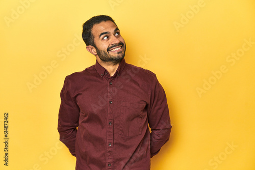 Casual young Latino man against a vibrant yellow studio background  relaxed and happy laughing  neck stretched showing teeth.