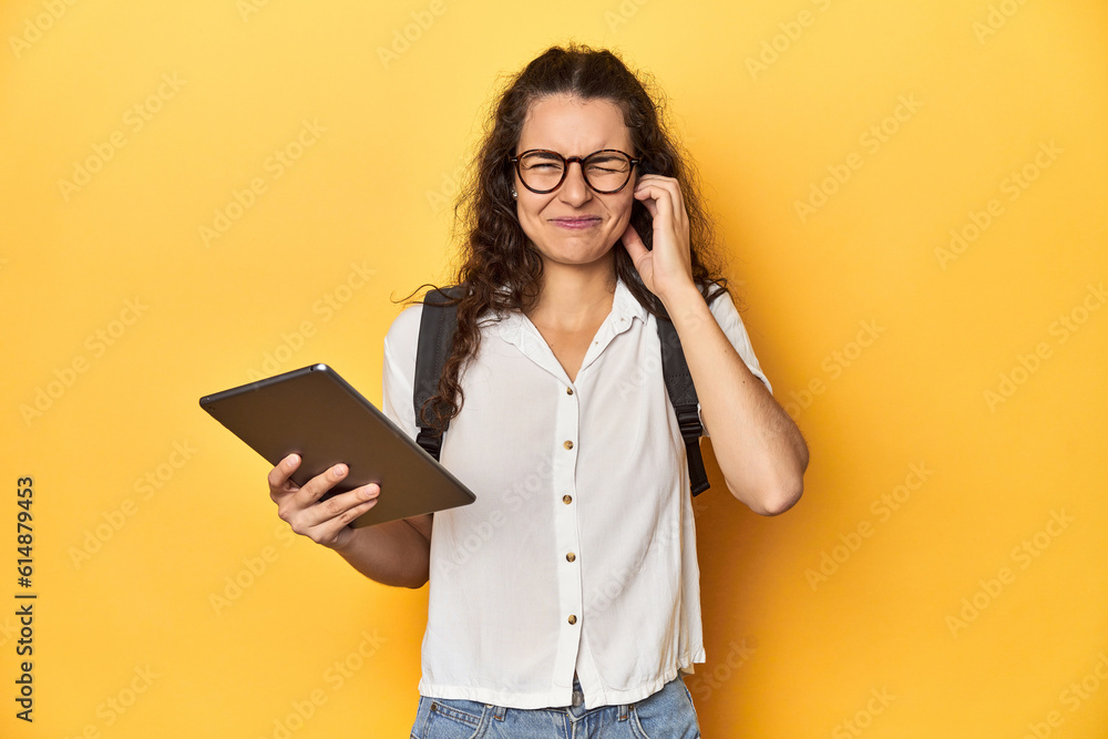 Student holding a tablet, glasses, backpack on, covering ears with hands. Student holding a tablet, glasses, backpack on, covering ears with hands.