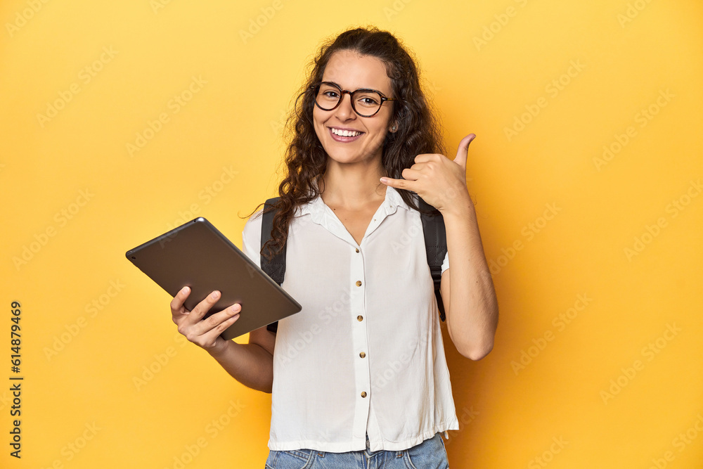Student holding a tablet, glasses, backpack on, showing a mobile phone call gesture with fingers. Student holding a tablet, glasses, backpack on, showing a mobile phone call gesture with fingers.