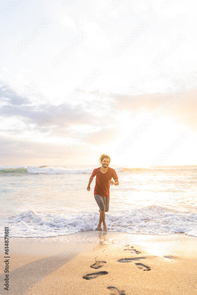 Vertical image of a smiling young man running through the waves at the shore of the beach on a summer day with beautiful sunset light. Vertical image of a smiling young man running through the waves at the shore of the beach on a summer day with beautiful sunset light.