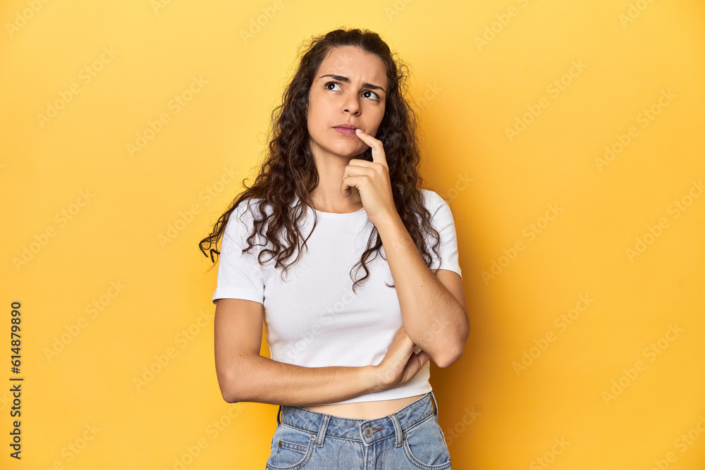 Young Caucasian woman, yellow studio background, looking sideways with doubtful and skeptical expression. Young Caucasian woman, yellow studio background, looking sideways with doubtful and skeptical expression.