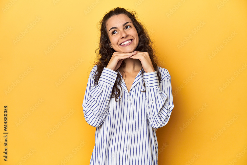Young Caucasian woman, yellow studio background, keeps hands under chin, is looking happily aside. Young Caucasian woman, yellow studio background, keeps hands under chin, is looking happily aside.