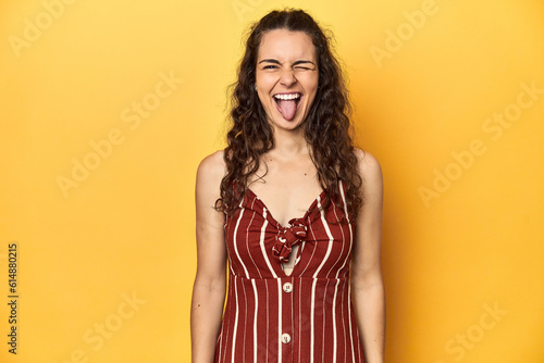 Young Caucasian woman, yellow studio background, funny and friendly sticking out tongue.