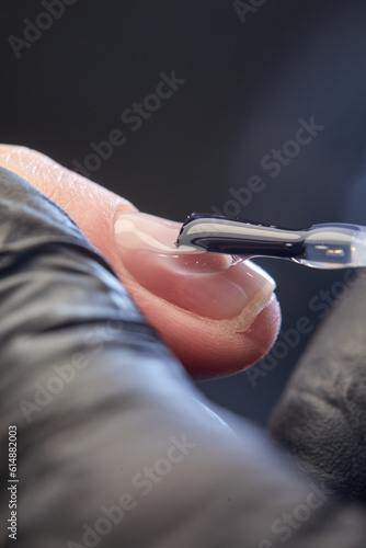 the master makes a manicure with a gel polish coating for a woman with clean nails. a master in black latex gloves paints a nail with transparent varnish