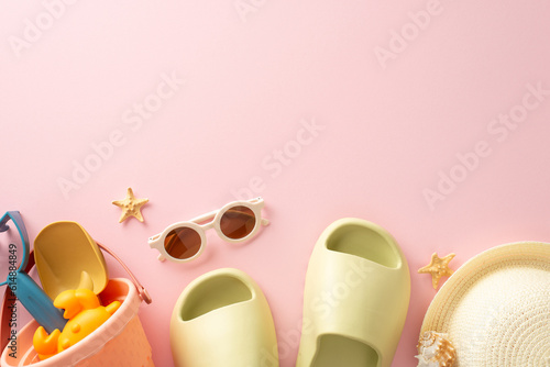 Relaxation by the sea with children concept. Top view snapshot capturing marine shells, sand toys, panama, slippers and sunglasses on pastel pink background. Empty space for text