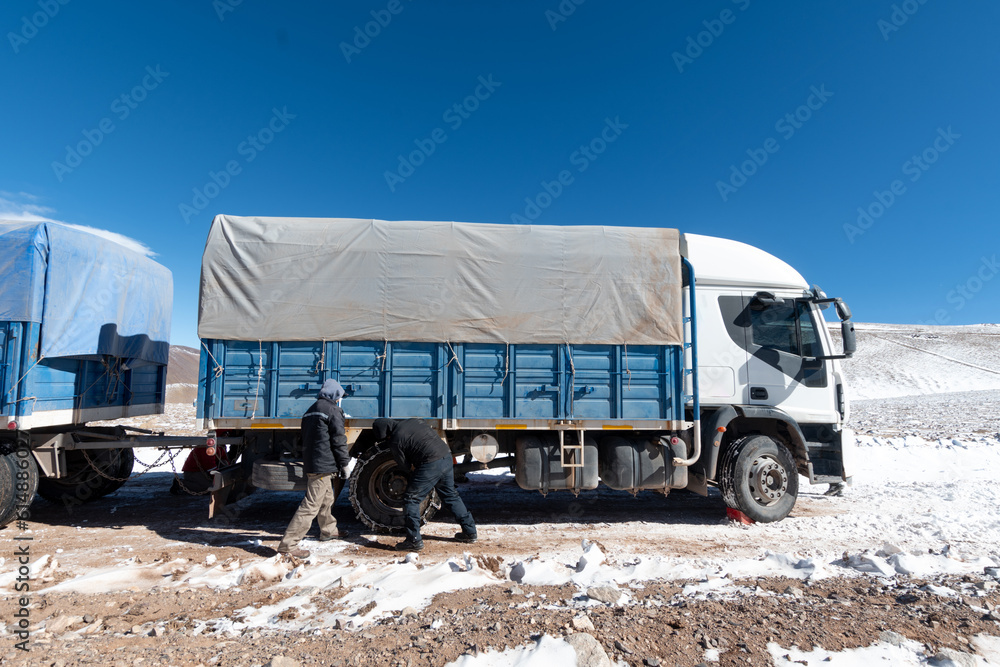 Workers putting chains on truck tires to climb a snowy mountain road. Argentinean mountain range.