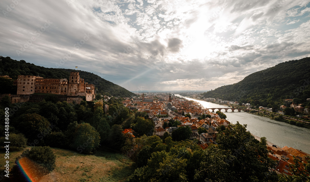 Aerial drone view over famous city of Heidelberg Germany with bridge on river Neckar. Dramatic cloudy sky with sunbeams over old town and mountains