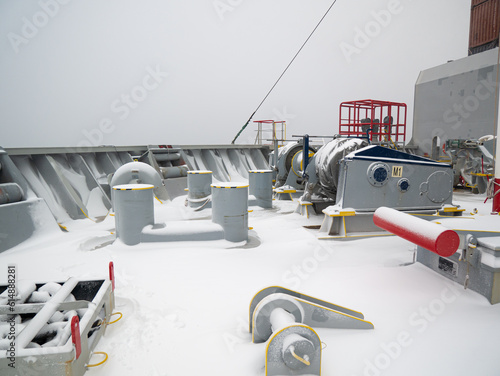 Forward part, panama central and roller fairleads for towing, bollards and winches with stored mooring lines of ultra large container ship and pacific ocean water  view during bad snowy weather. photo