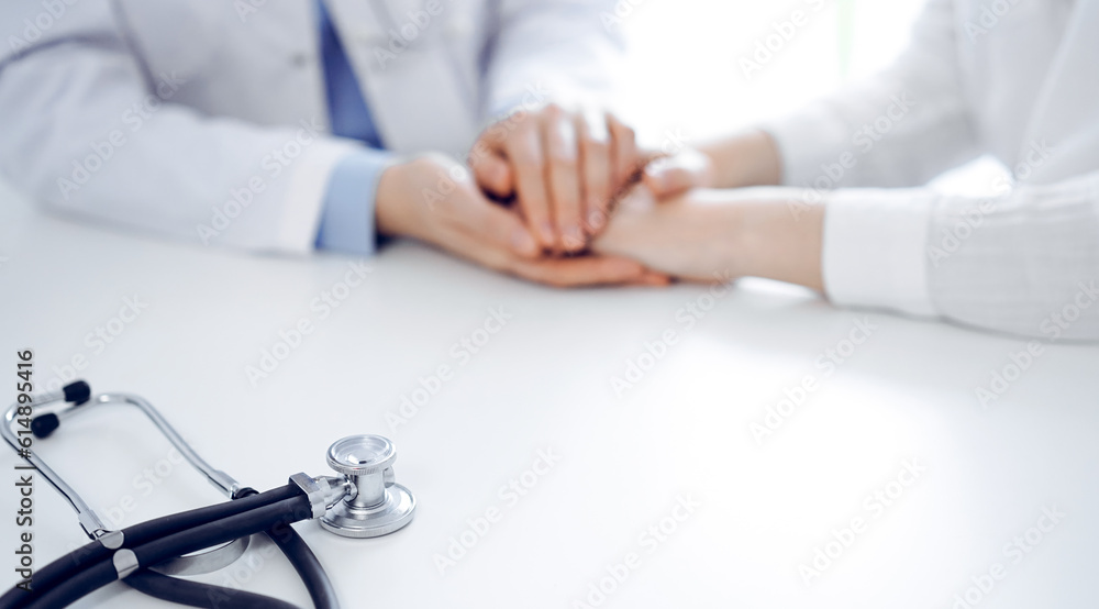 Stethoscope lying on the tablet computer in front of a doctor and patient sitting near each other. Medicine, reassuring hands concept