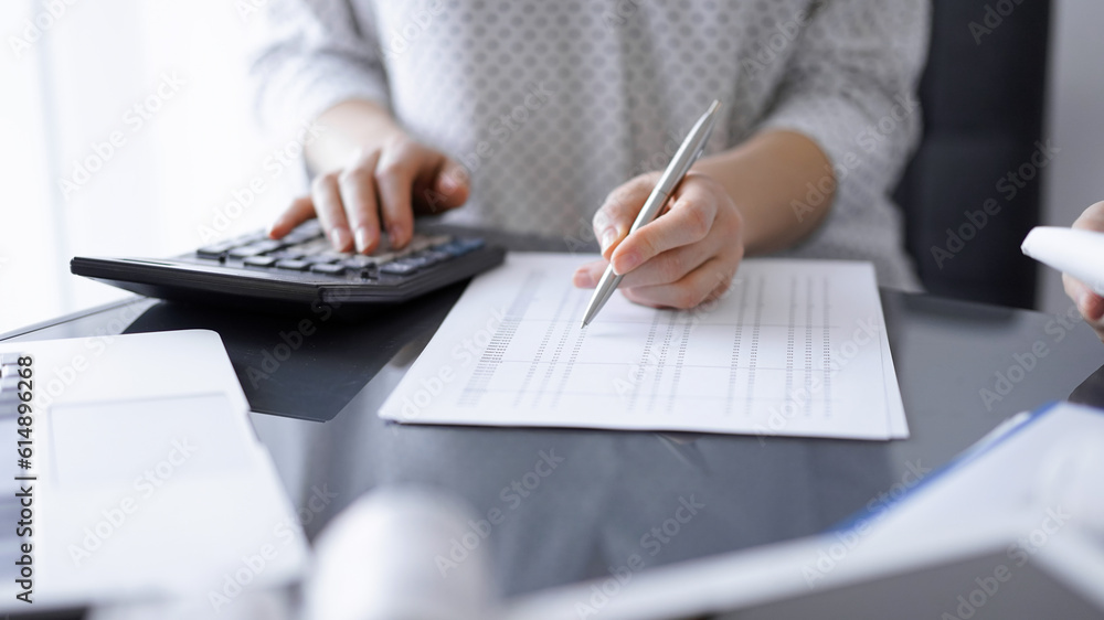 Woman accountant using a calculator and laptop computer while counting taxes with a client or colleague. Business audit team Woman accountant using a calculator and laptop computer while counting taxes with a client or colleague. Business audit team