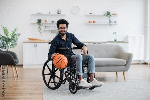 Фотография Cheerful bespectacled adult with mobility impairment dribbling ball in studio apartment on weekend