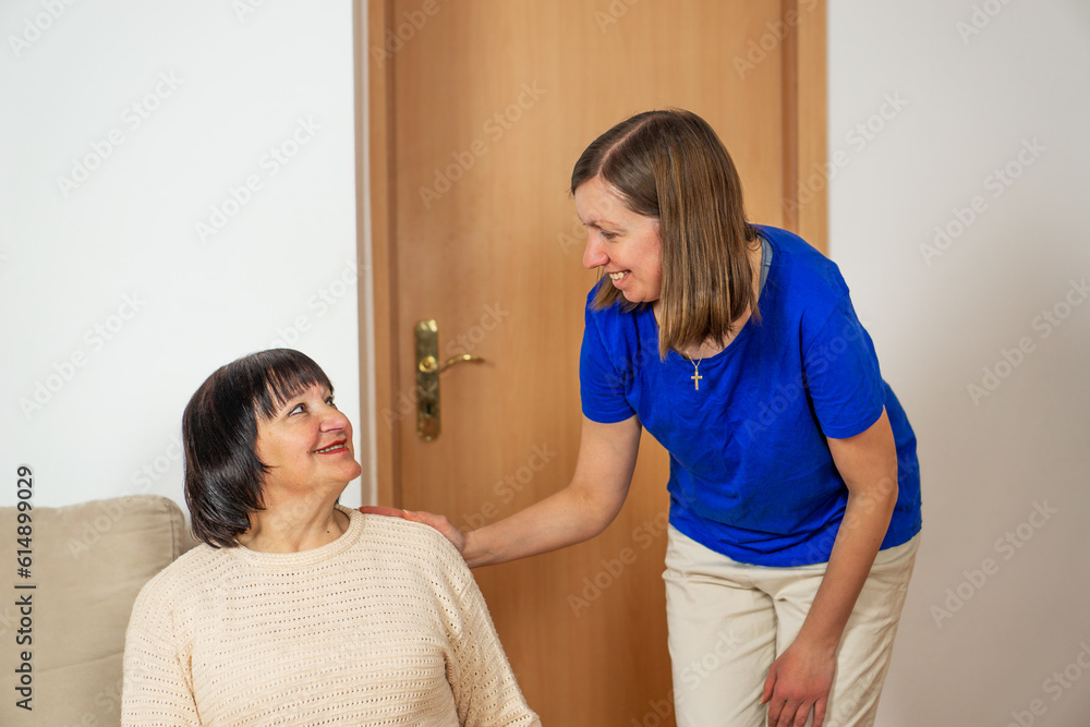 Obraz premium Young caregiver helping senior woman at home. Caring nurse assisting her middle aged female patient.