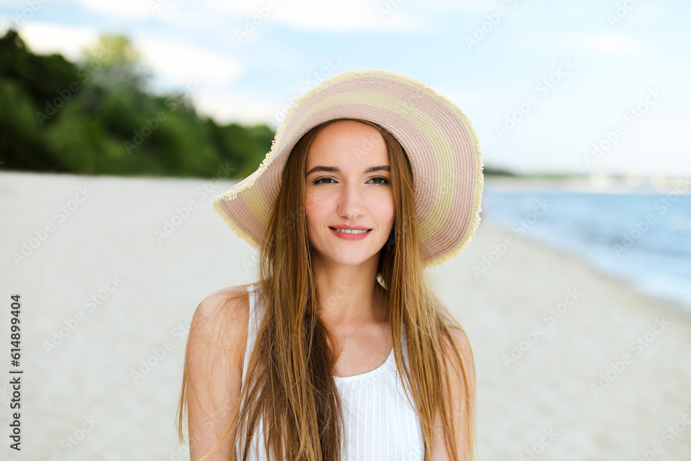 Portrait of a happy smiling woman in free happiness bliss on ocean beach standing with a hat. A female model in a white summer dress enjoying nature during travel holidays vacation outdoors