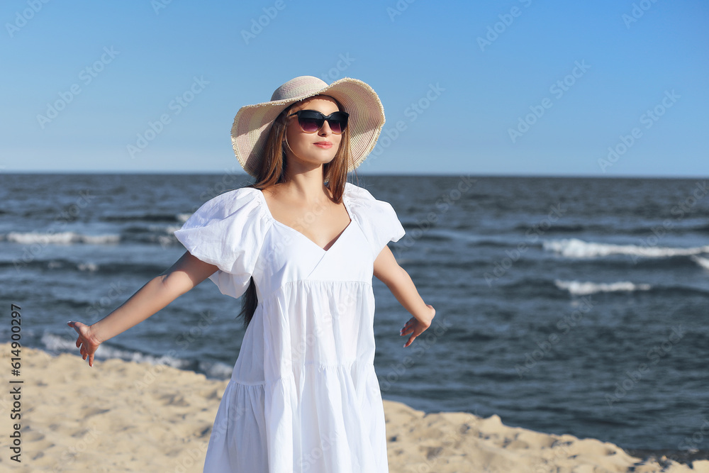 Happy blonde woman is on the ocean beach in a white dress and sunglasses, open arms