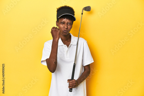 African golfer woman with her golf club, sports concept, showing fist to camera, aggressive facial expression.