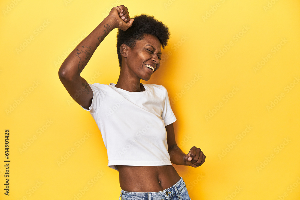 African woman, white tee, short hair, yellow studio, celebrating a special day, jumps and raise arms with energy. African woman, white tee, short hair, yellow studio, celebrating a special day, jumps and raise arms with energy.