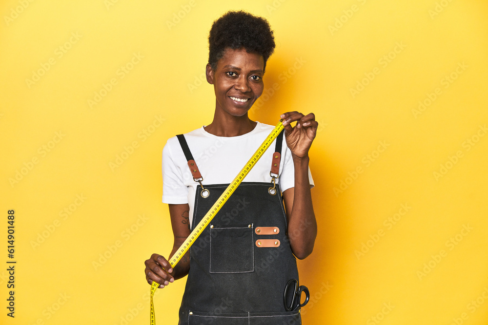 African tailor woman with measuring tape, yellow studio background. African tailor woman with measuring tape, yellow studio background.
