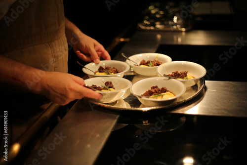 Pequenos pratos de carne picadinha com purê de mandioquinha, sendo finalizados por um chef talentoso, prontos para serem servidos em um elegante evento social.