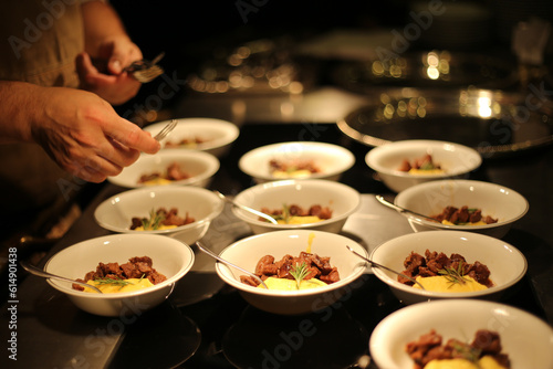 Pequenos pratos de carne picadinha com purê de mandioquinha, sendo finalizados por um chef talentoso, prontos para serem servidos em um elegante evento social.