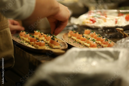 Um talentoso chef finalizando um aperitivo sofisticado de salmão sobre torradinhas, adicionando temperos verdes frescos, em um elegante evento social. photo