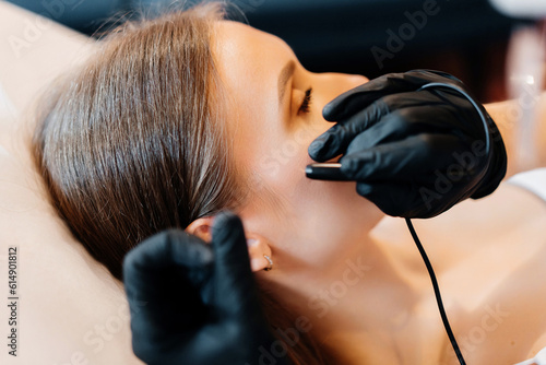 Close up view of doctor is doing electroepilation to the client, using electro needle and tweezers. Hair removal procedure, professional beauty care. Beautcian's hands in gloves. High quality photo photo