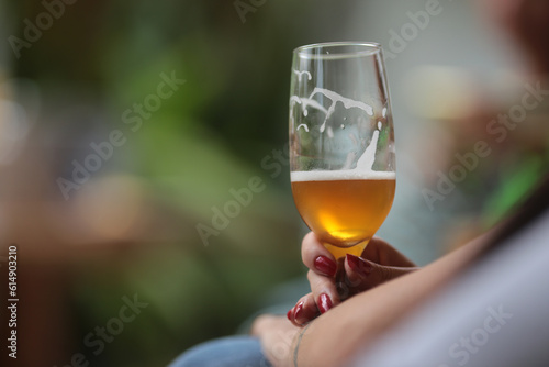 Mão feminina segurando uma taça de cerveja em um evento social animado.