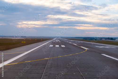 At the airport, endless runway extends into the horizon, featuring prominent aircraft markings and well-defined pathways for the safe arrival and departure of planes at sunset © vladim_ka