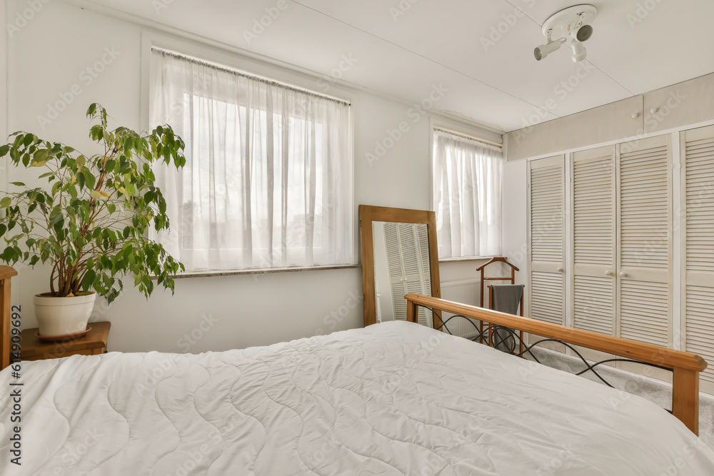 a bed in a bedroom with white sheets and curtains on the window behind it is a plant that looks like a tree a bed in a bedroom with white sheets and curtains on the window behind it is a plant that looks like a tree