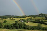 Landscape of rural County Leitrim, Ireland featuring farm nestled amongst rolling hills of farmland pastures against backdrop of overcast skies with rainbow visible